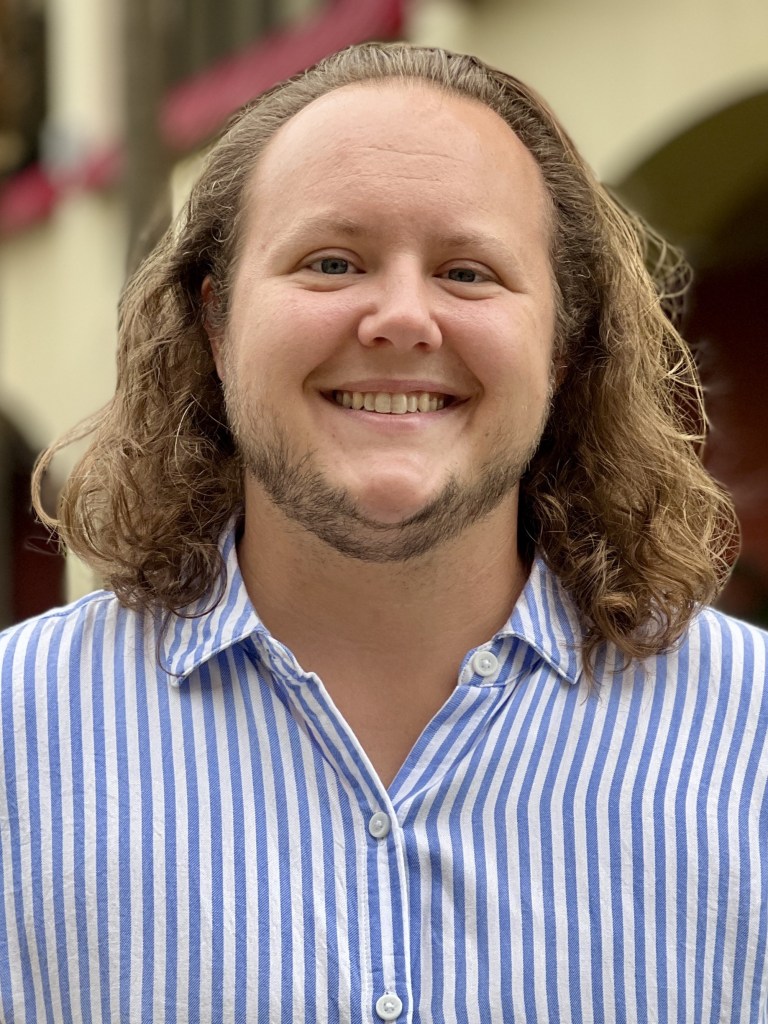 A photo of the creator, Al Weyant-Forbes smiling in the camera, wearing a shirt with blue stripes.
